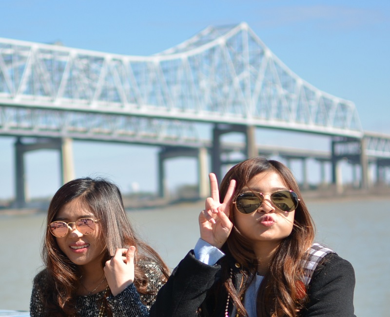 Women posing with peace sign and silly faces in front of Crescent City Connection Bridge
